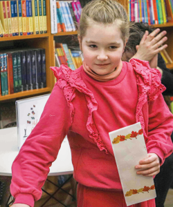 A young girl wearing an outfit of all pink holds a piece of paper in a circle of clapping people.