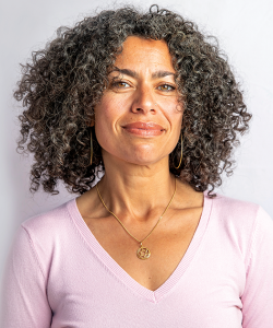 Kyla Kupferstein Torres is a mixed-race woman with medium-length curly hair. She wears a golden Star of David necklace and a pink long-sleeved v-neck shirt.