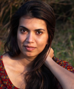 A sun-soaked portrait of Zara Chowdhary, a South Asian woman with long dark hair and tan skin. She wears a maroon scoop-neck top with a colorful pattern.